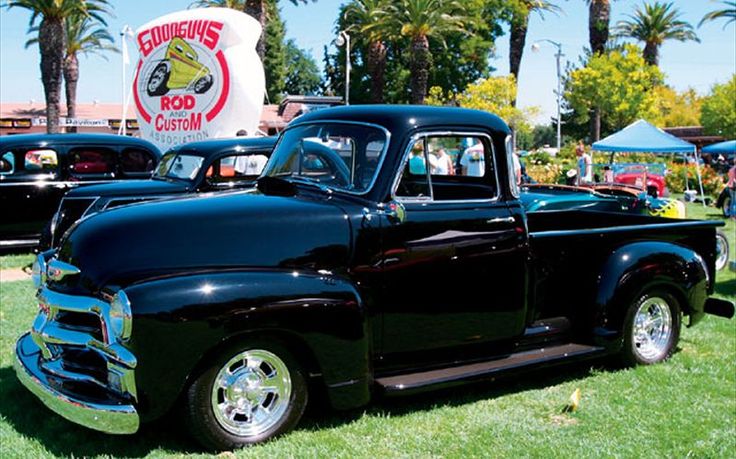 an old black pickup truck parked on top of a lush green field next to palm trees