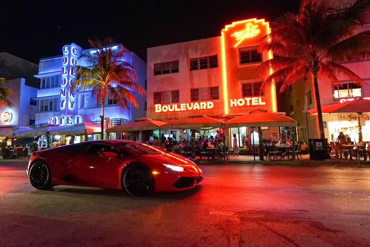 a red sports car parked in front of a hotel with neon lights on it's side