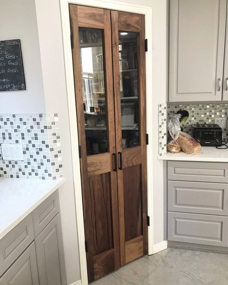 a kitchen with two wooden doors and white cabinets in the corner, along with a counter top