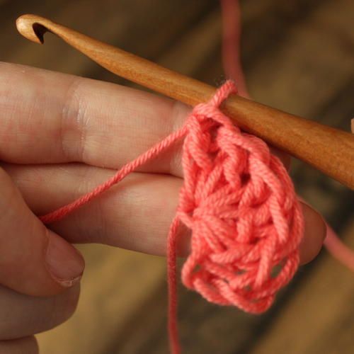 a person holding a crochet hook in their left hand and knitting yarn on the right