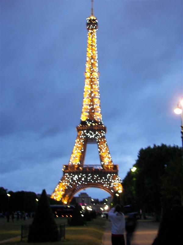 the eiffel tower lit up at night with people standing in front of it