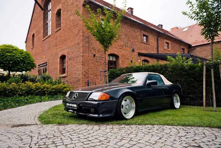 a black car is parked in front of a brick building with green grass and trees