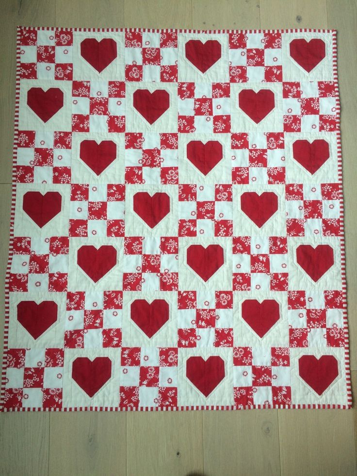 a red and white quilt with hearts on the front, sitting on a wooden floor