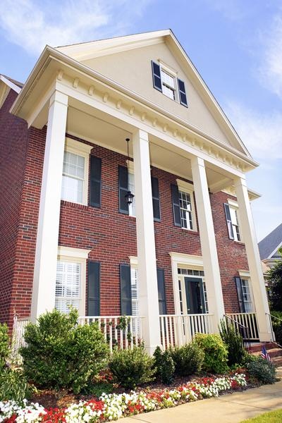 a large brick house with white columns and black shutters on the front porch, surrounded by flowers