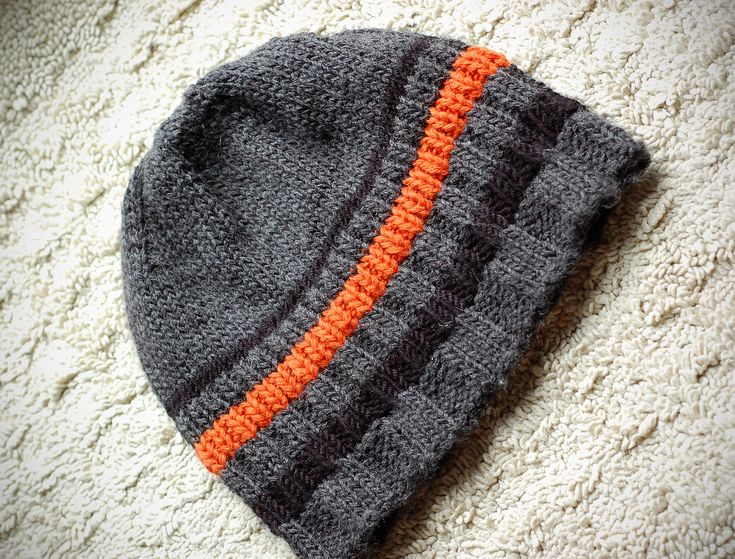 a gray and orange knitted hat laying on top of a white carpeted floor