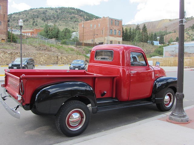 an old red truck is parked on the side of the road next to a street light