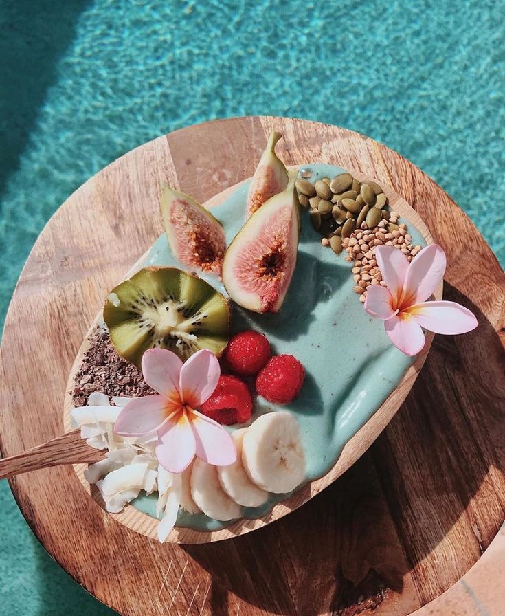 there is a cake with fruit and flowers on the table next to the pool,