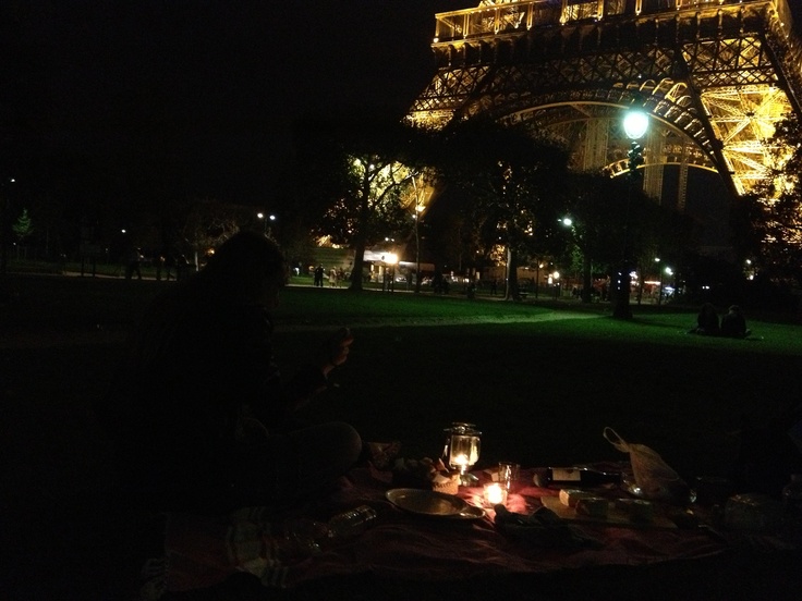 the eiffel tower is lit up at night with people sitting in front of it