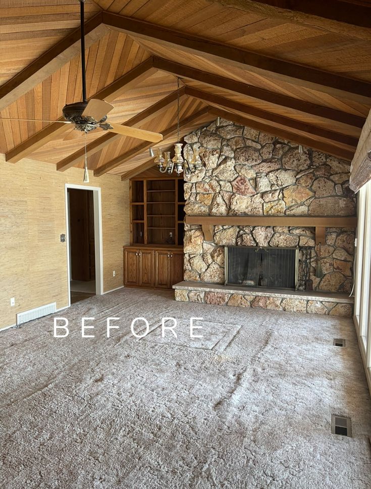 an empty living room with stone fireplace and ceiling fan