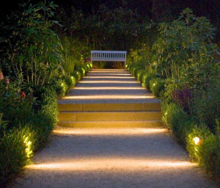 a white bench sitting in the middle of a lush green park at night with lights on it's sides