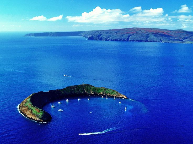 an island in the middle of the ocean with boats floating on it's surface