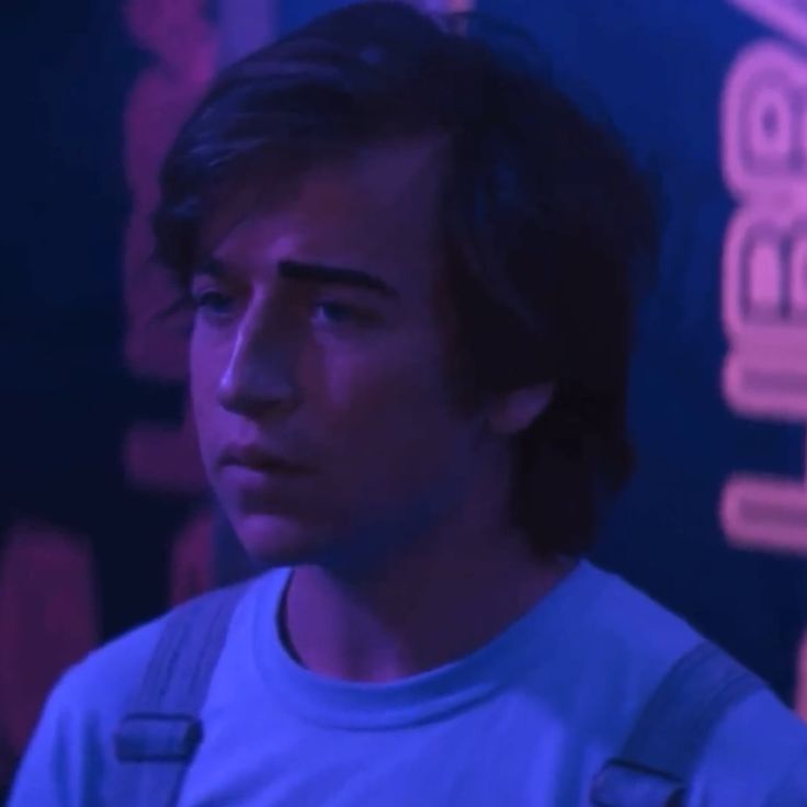 a young man standing in front of a blue wall with neon lights on it's sides