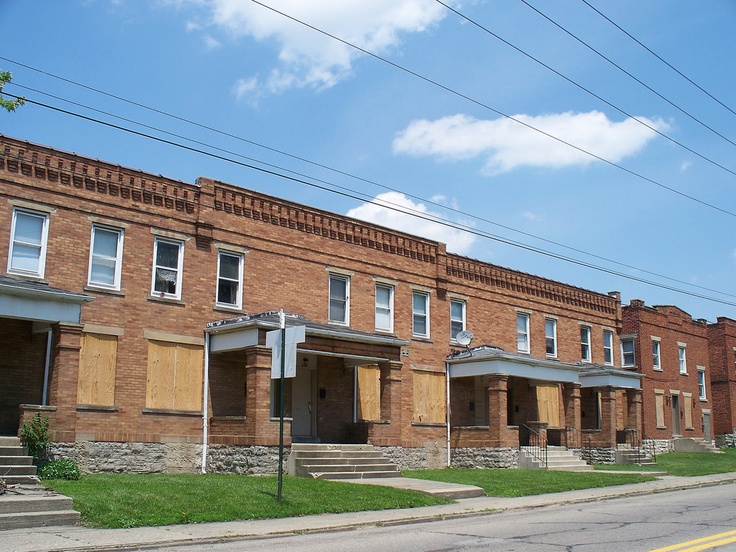 an empty street in front of some brick buildings with boarded up windows and shutters