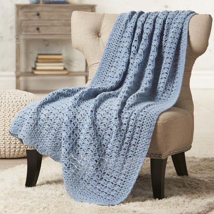 a blue crocheted blanket sitting on top of a chair next to a white rug