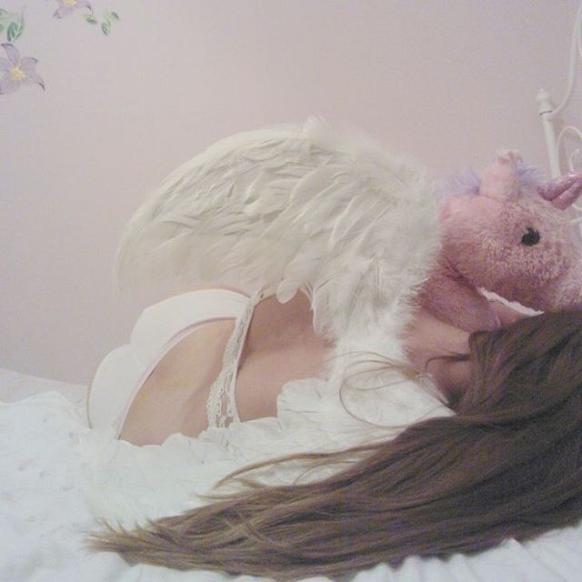 a woman laying on top of a bed next to a pink stuffed animal and angel wings