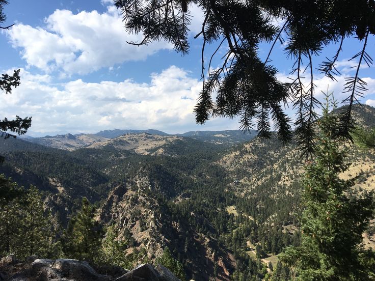 a view from the top of a mountain with trees and mountains in the foreground