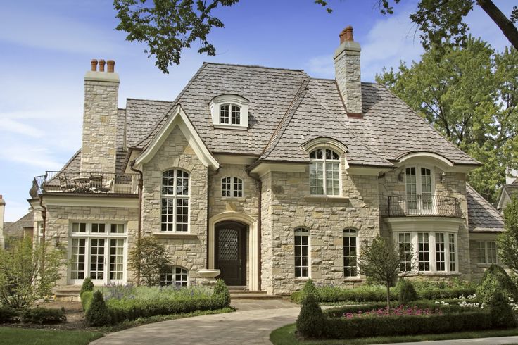 a large stone house with lots of windows and bushes around it's front entrance