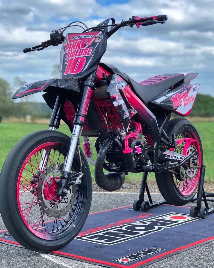 a pink and black dirt bike parked on top of a parking lot next to a field