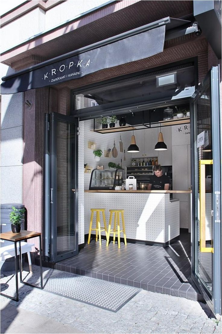 a small coffee shop with yellow stools in front of the counter and open door