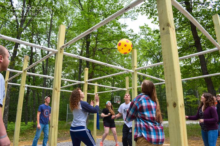 a group of people playing with a yellow ball in a playground area surrounded by trees