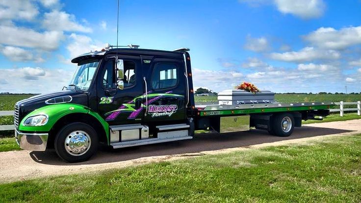 a green and black tow truck driving down a dirt road next to a white fence