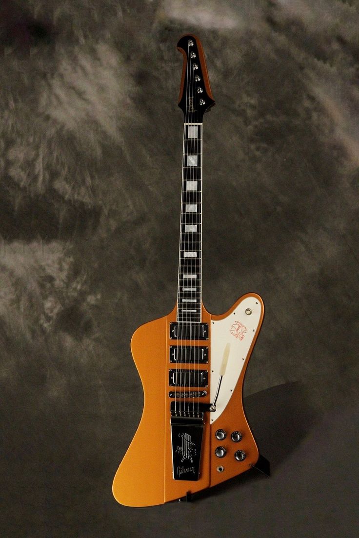 an orange electric guitar sitting on top of a black surface with clouds in the background