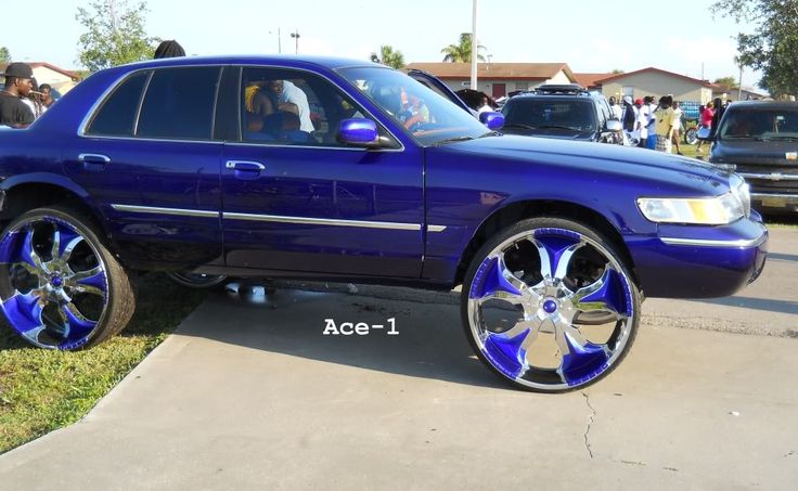 a blue suv parked on the side of a road next to other cars and people