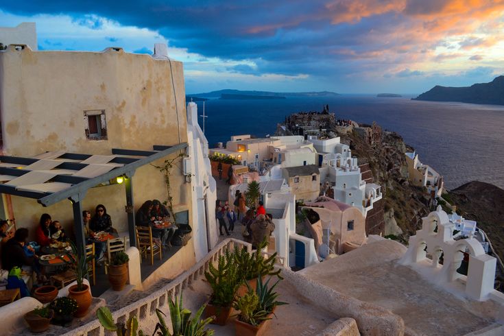 people are gathered on the balcony of an old building overlooking the ocean and cliffs at sunset