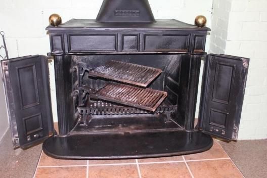 an old fashioned fireplace with two doors and a stove top on the floor next to it