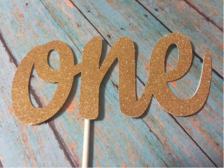 a cake topper with the word one on it in gold glitter and sitting on a wooden table