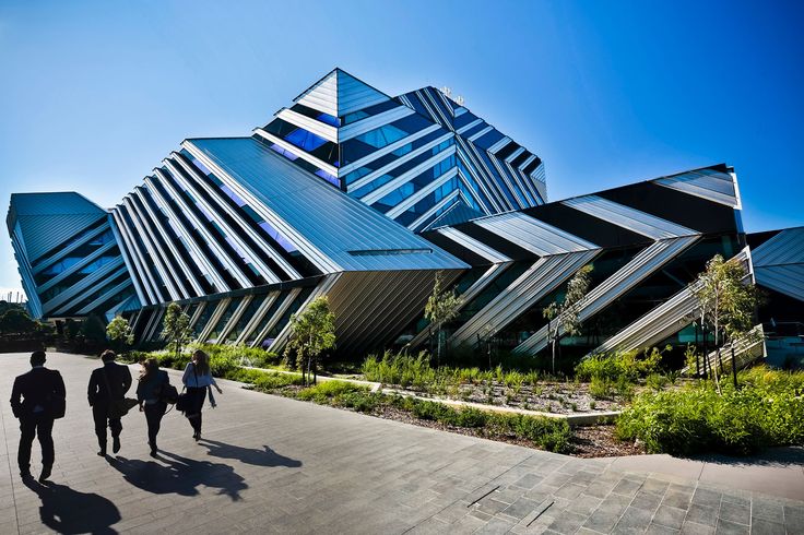 three people walking in front of a building that looks like an abstract structure with many windows