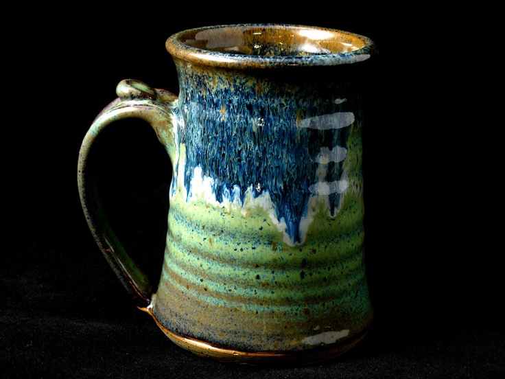 a green and blue coffee mug sitting on top of a black table next to a wall