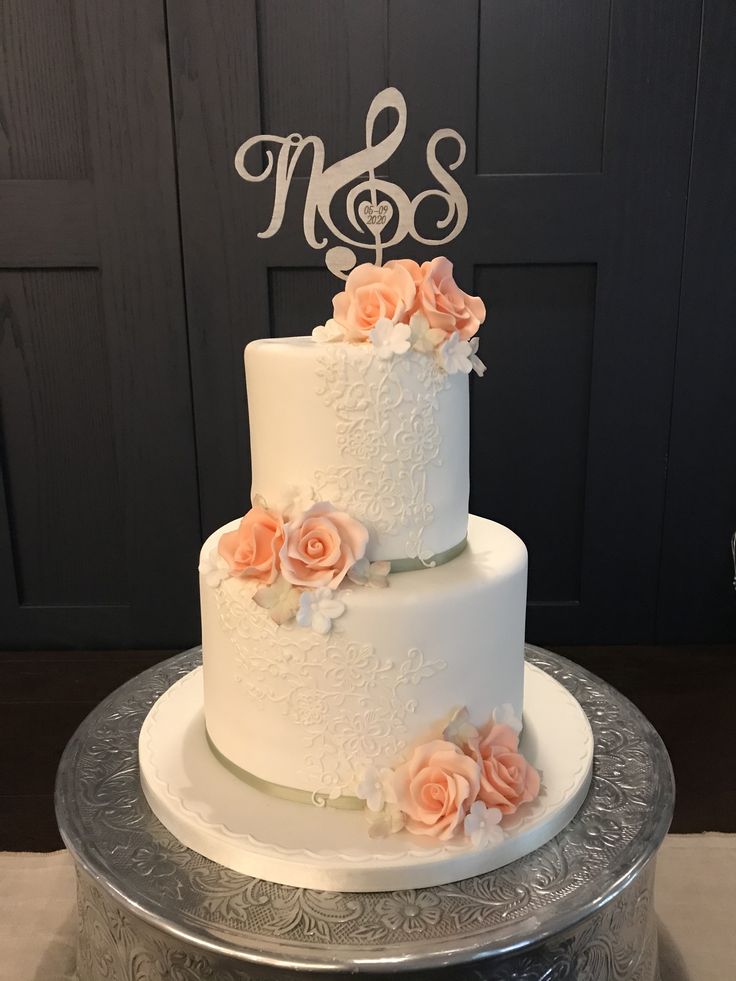 a white wedding cake with pink flowers and a monogrammed topper on a silver platter