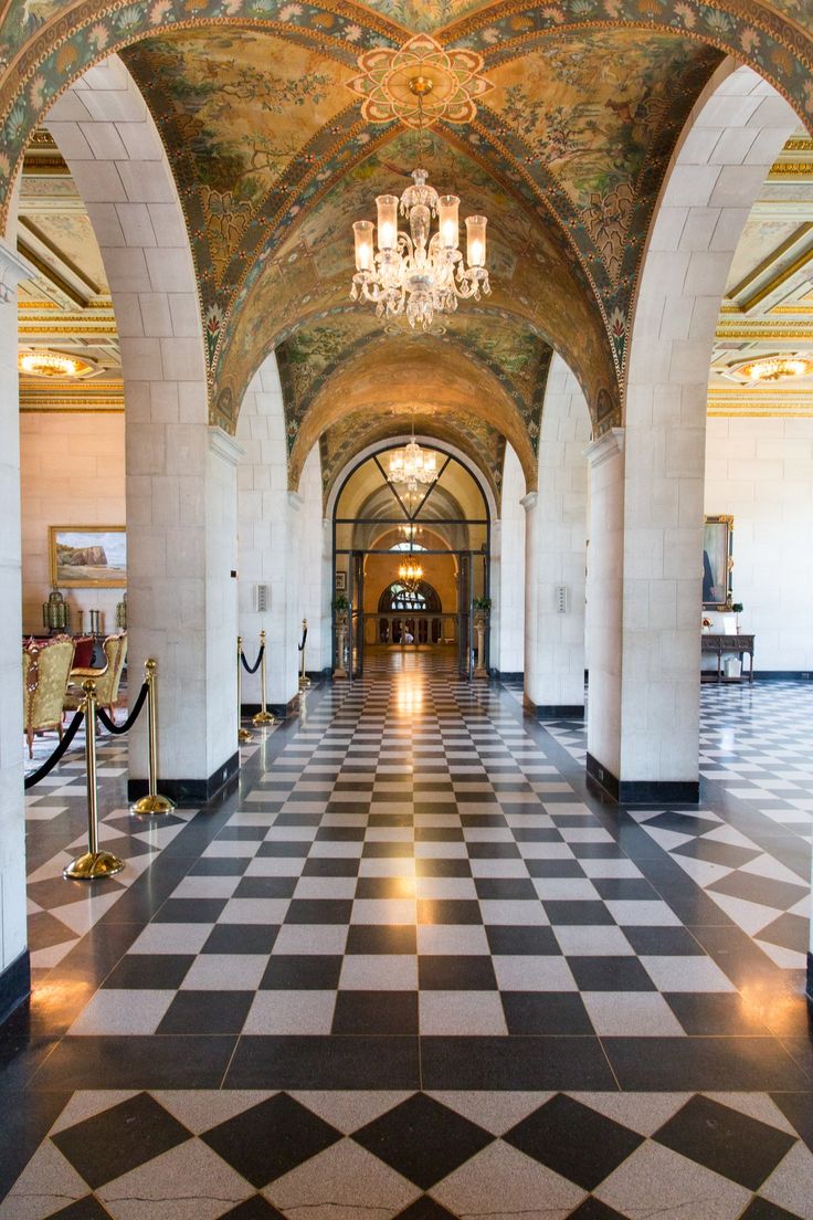 an ornate hallway with black and white checkered flooring, chandelier and paintings on the walls