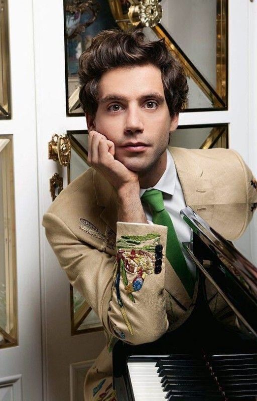 a man in a suit and tie leaning on a piano