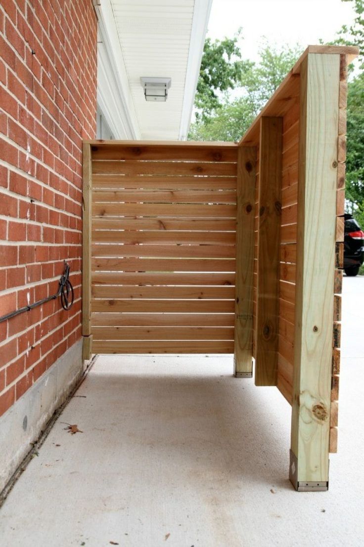 an open wooden gate on the side of a brick building next to a sidewalk and trees