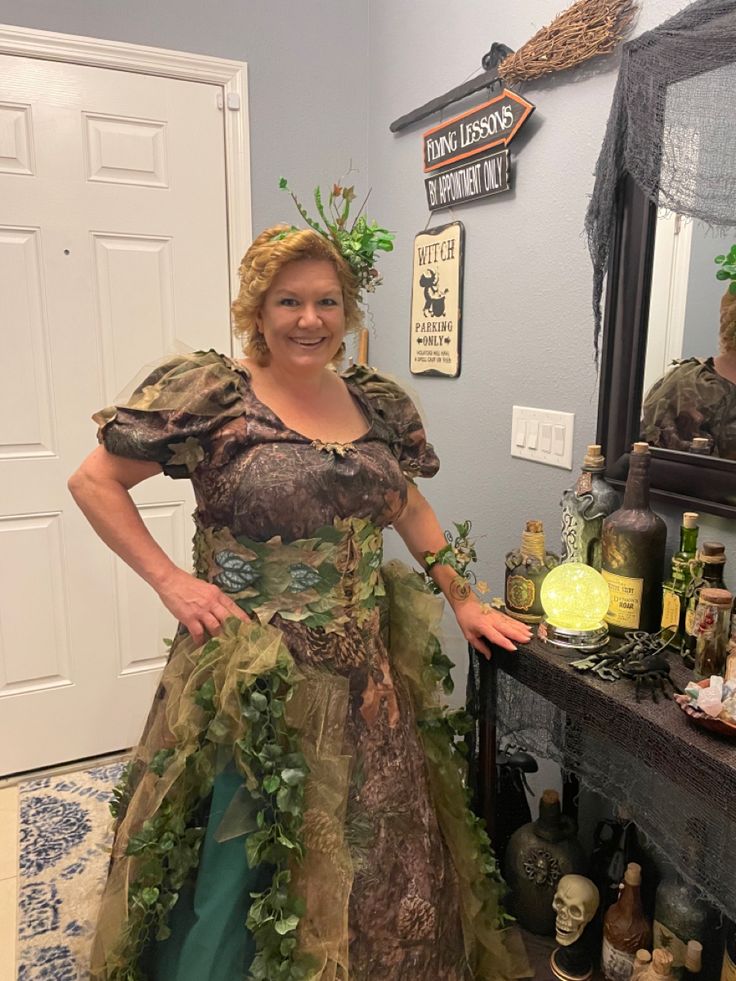 a woman in a costume standing next to a table full of liquor bottles and plants