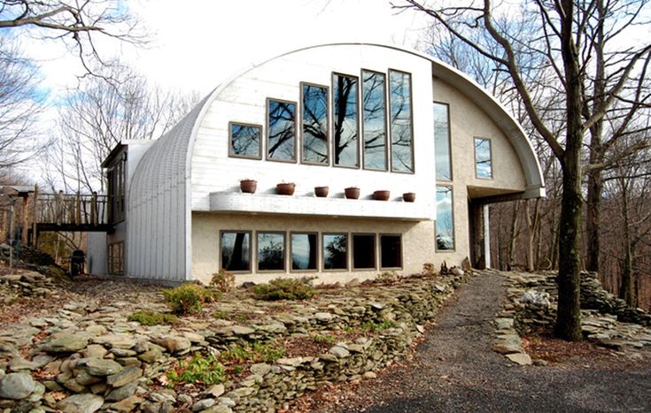 a large white house sitting in the middle of a forest next to a stone wall