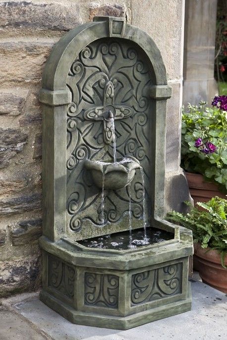 a water fountain in front of a building with potted plants and flowers around it