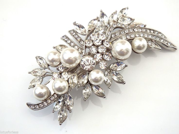 a brooch with pearls and crystal stones on it's side, sitting on a white surface