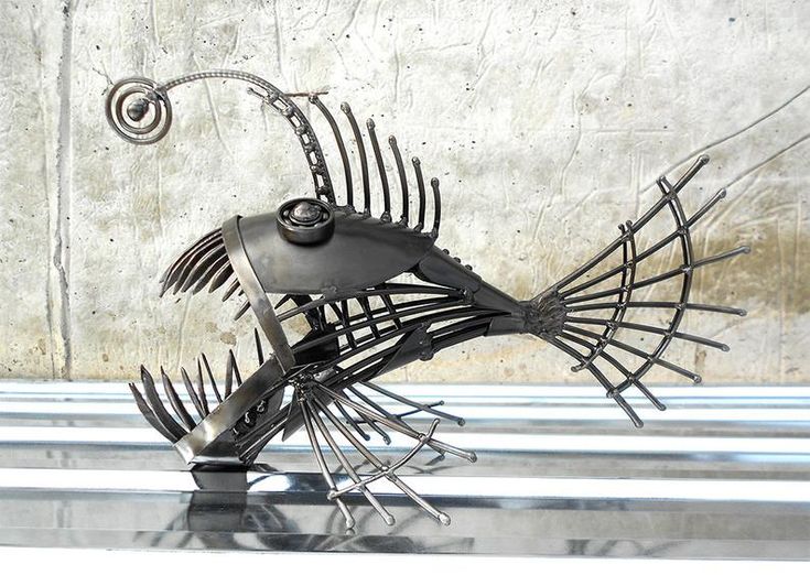 a metal fish sculpture sitting on top of a black table next to a white wall