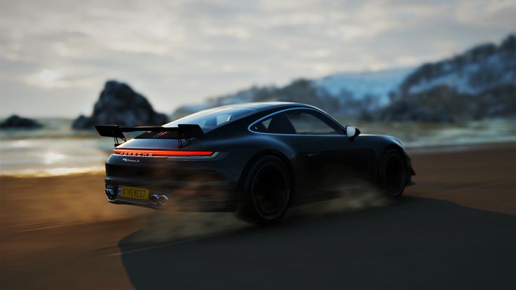 a black sports car driving down a road next to the ocean on a cloudy day