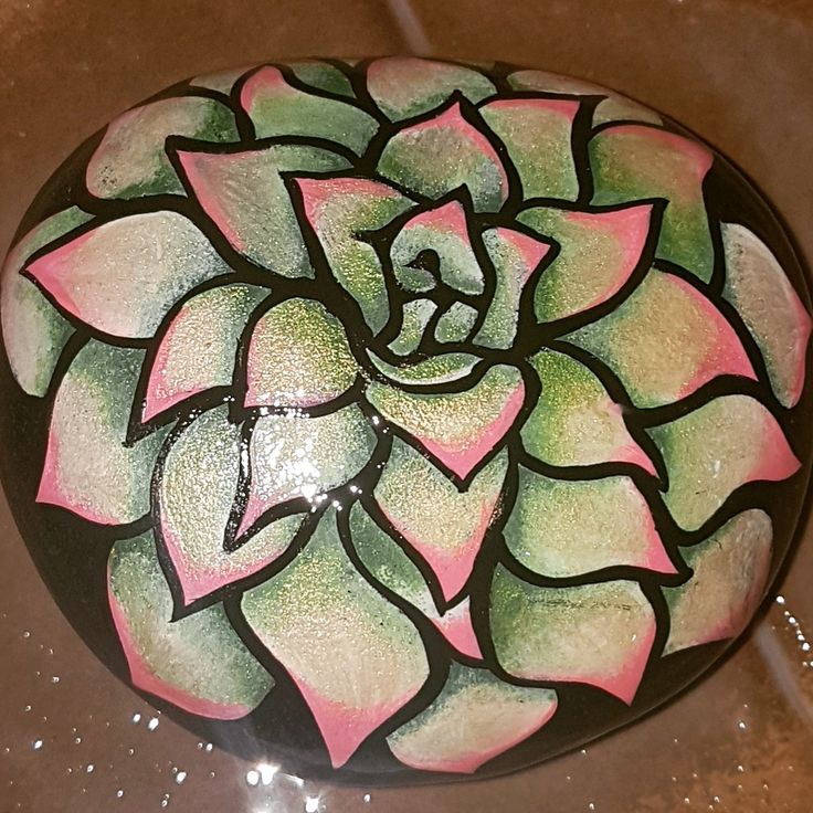 a painted rock with a pink and green flower on it's side sitting on a tile floor