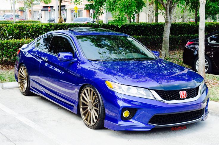 a blue car is parked in a parking space next to some bushes and trees on the sidewalk