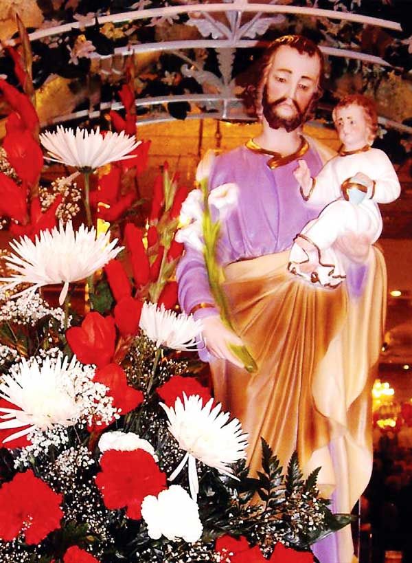 a statue of jesus holding a child surrounded by flowers