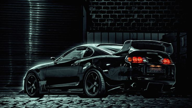 a black sports car parked in front of a brick building with its trunk open and lights on