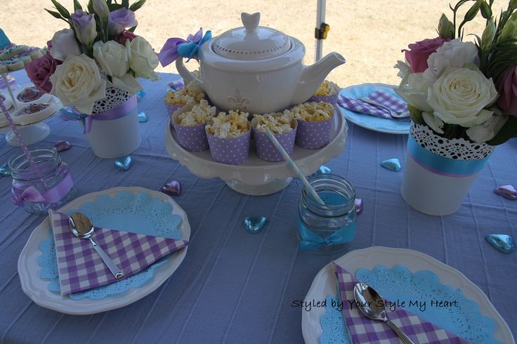 a table set up for a tea party with purple and white decorations, blue gingham