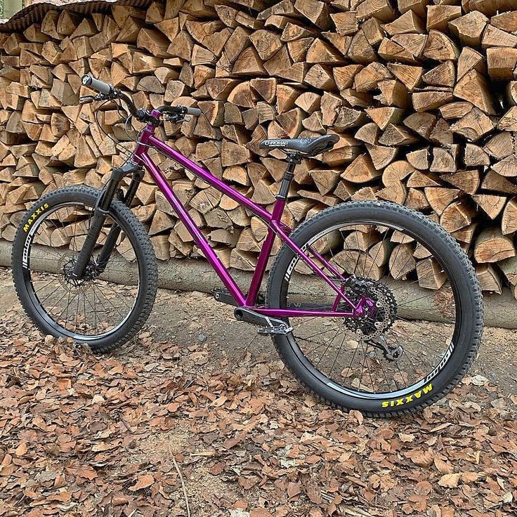 a purple bike parked next to a pile of logs