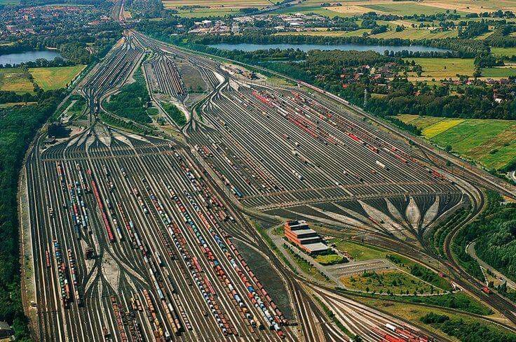 an aerial view of a train yard with many trains on the tracks and trees in the background