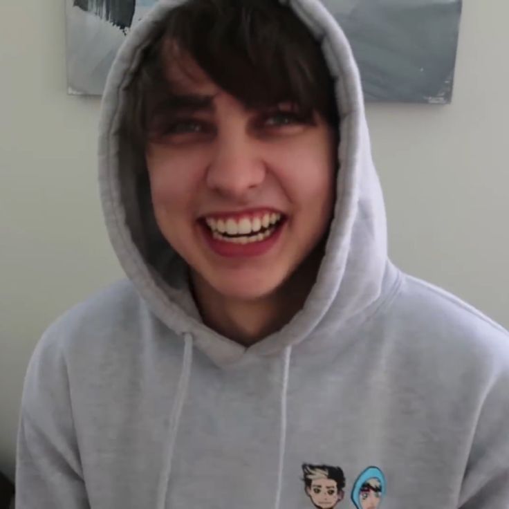 a young man wearing a grey hoodie and smiling at the camera with his mouth open